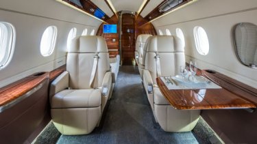 An interior of a business jet with two cream seats and a wooden table.